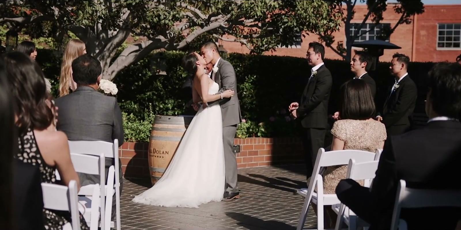 Andrea and Gene kissing at the end of the ceremony in the courtyard, guests seated and a wine barrel beside them.