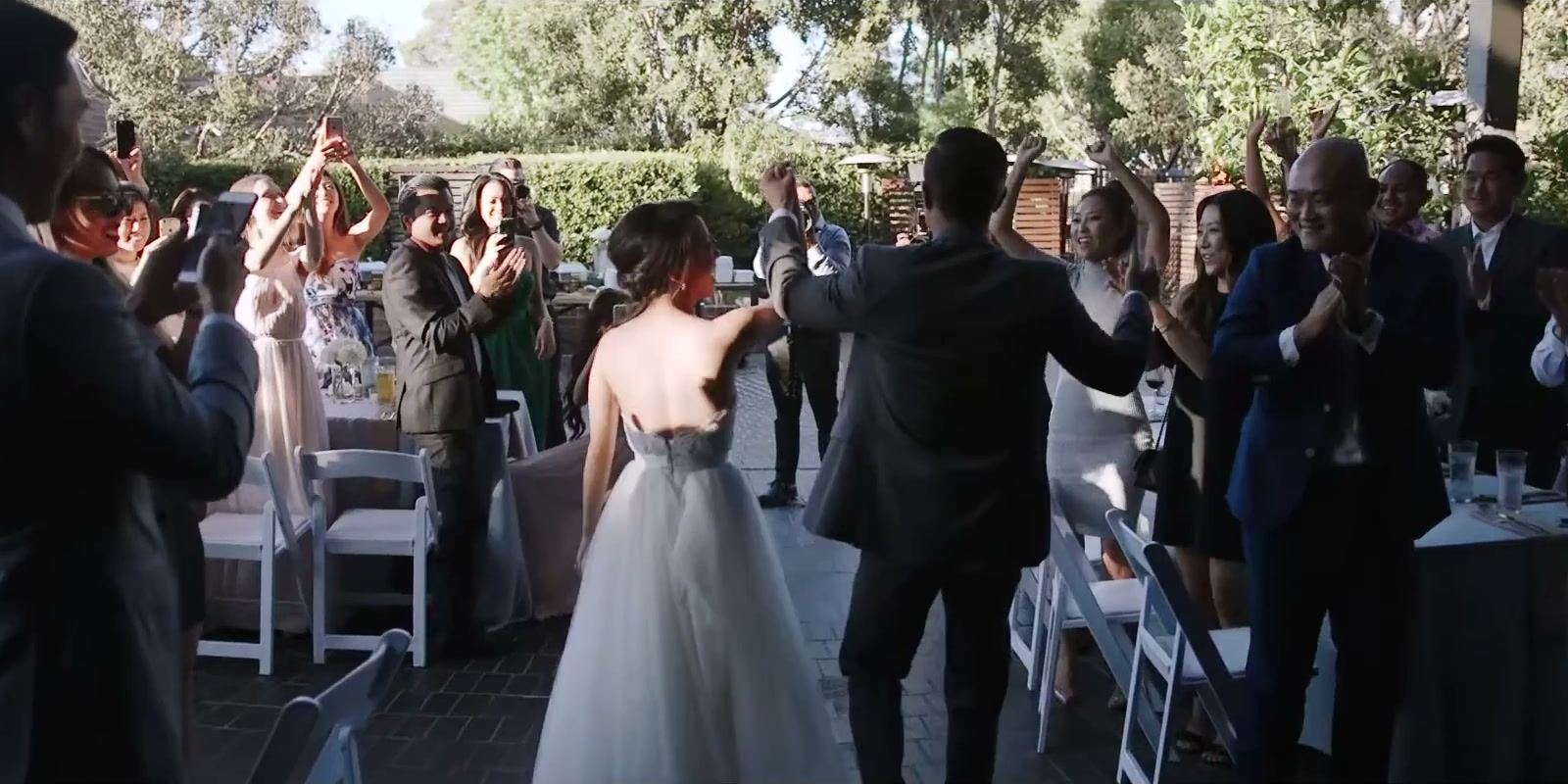 Guests cheering as Andrea and Gene walk between the tables in the garden.