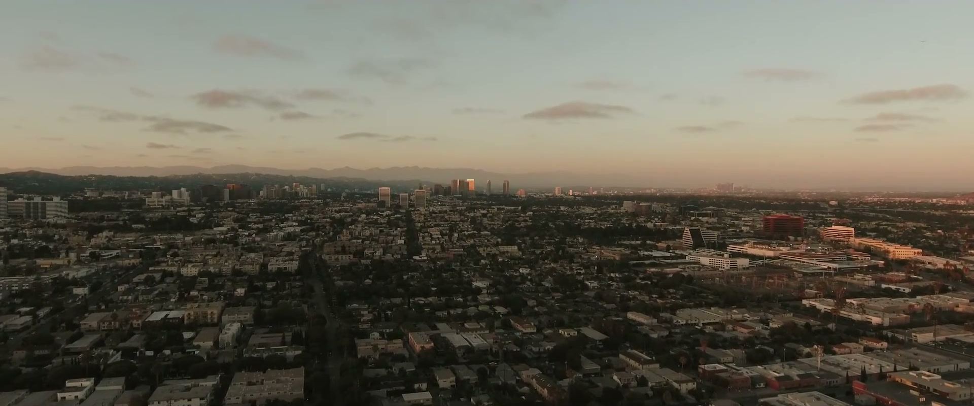 The city from above at dusk, rows of low buildings running out toward distant towers.