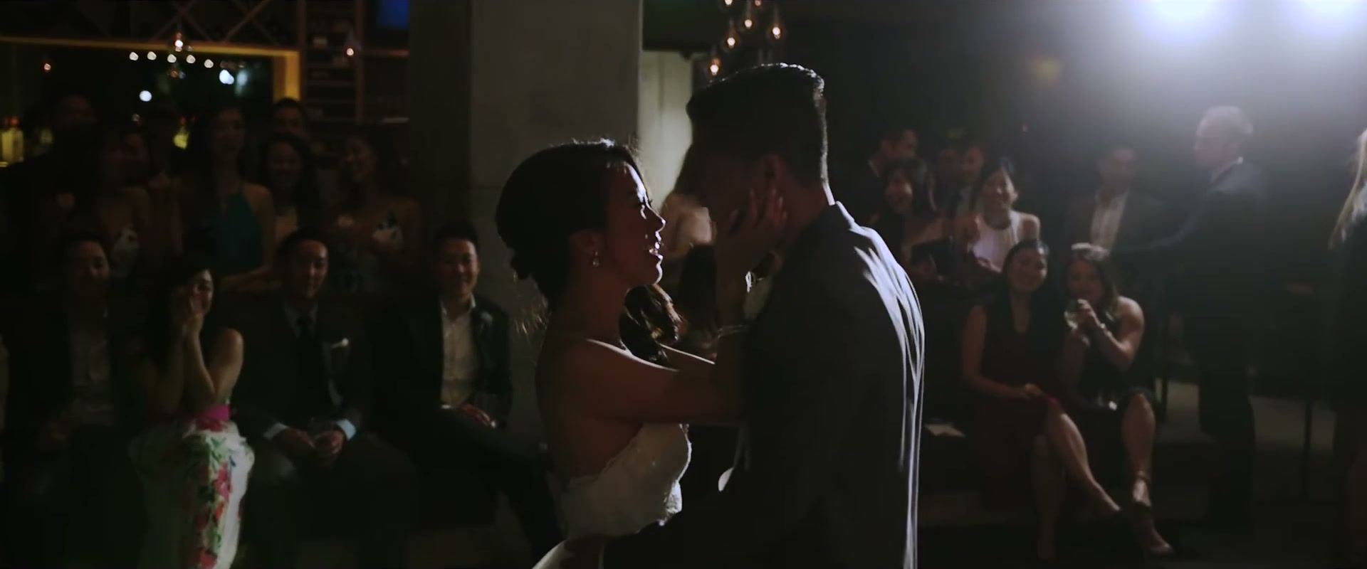 Andrea and Gene close on the dance floor at night, guests watching from the dark around them.