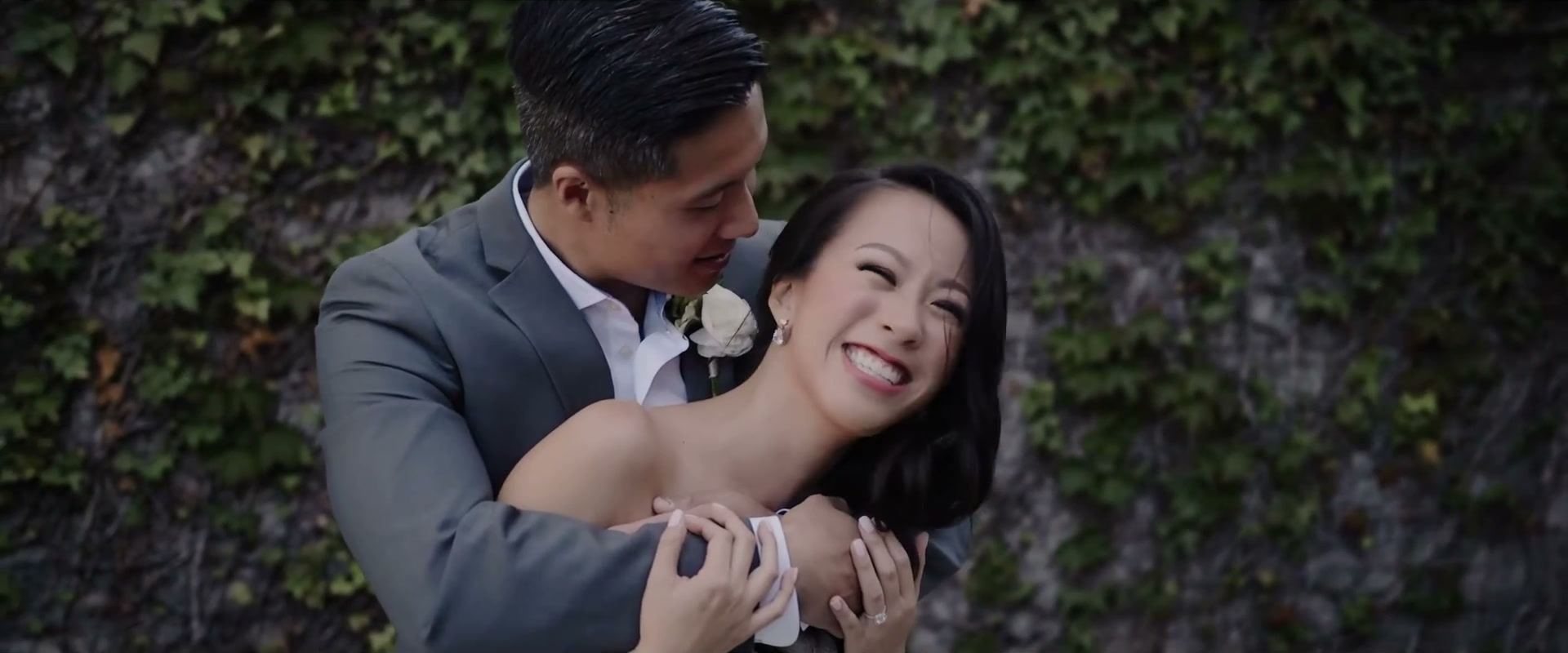 Gene holding Andrea from behind as she laughs, an ivy-covered wall behind them.