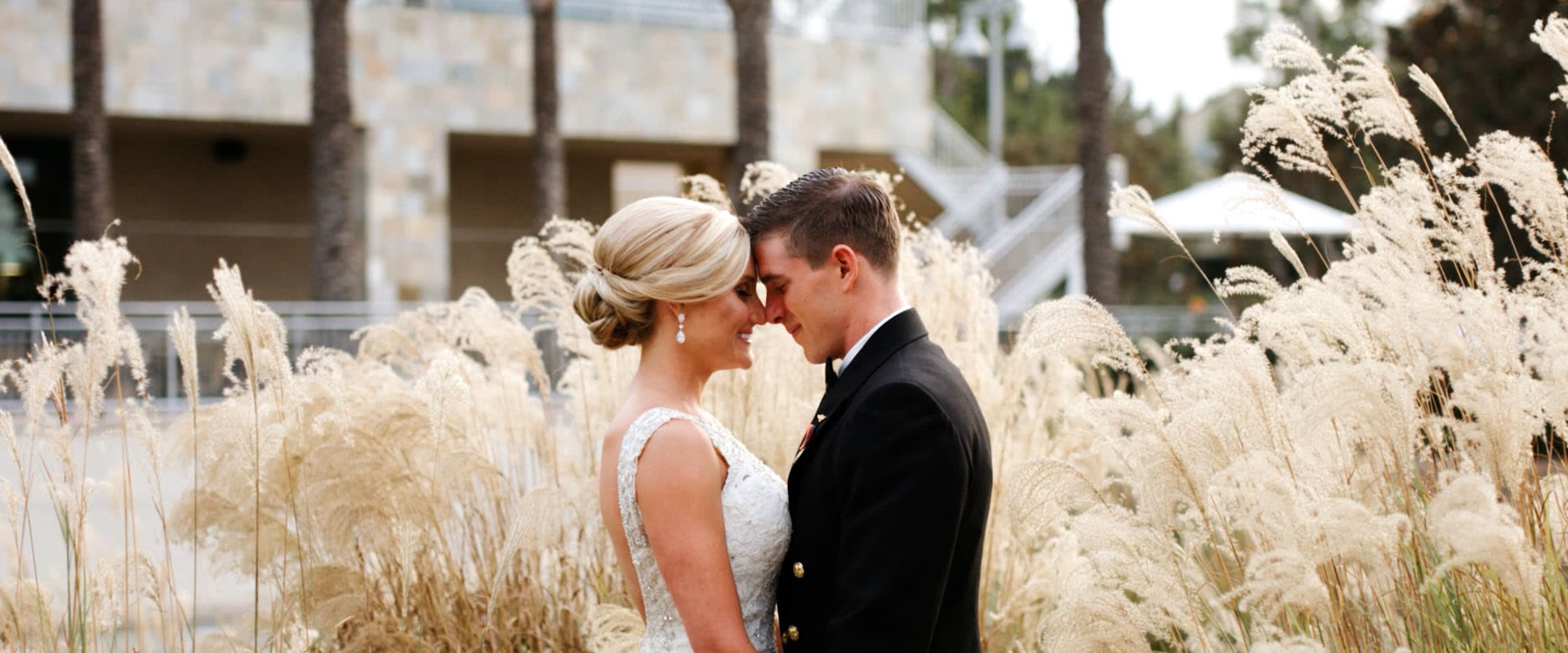 Andrew and Kendal forehead to forehead among tall ornamental grasses at golden hour in Irvine