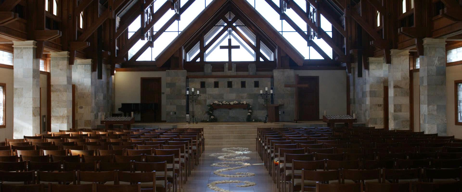 The Mariners Church sanctuary in Irvine, a timber A-frame with clerestory glazing, stone columns and a rose petal aisle set for a wedding ceremony