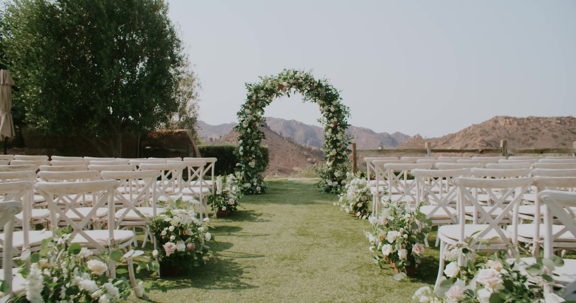 The ceremony arch and rows of white chairs on the lawn at Cielo Farms, with the Malibu mountains behind
