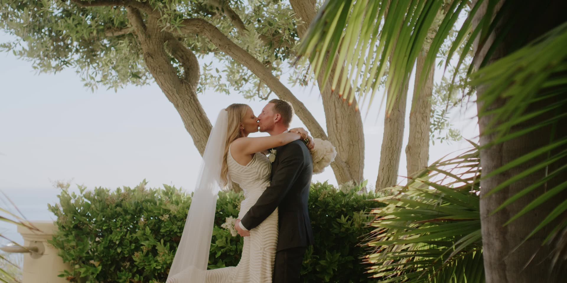 Adam and Laura kissing beneath the trees with the Pacific behind them at The Ritz-Carlton, Laguna Niguel