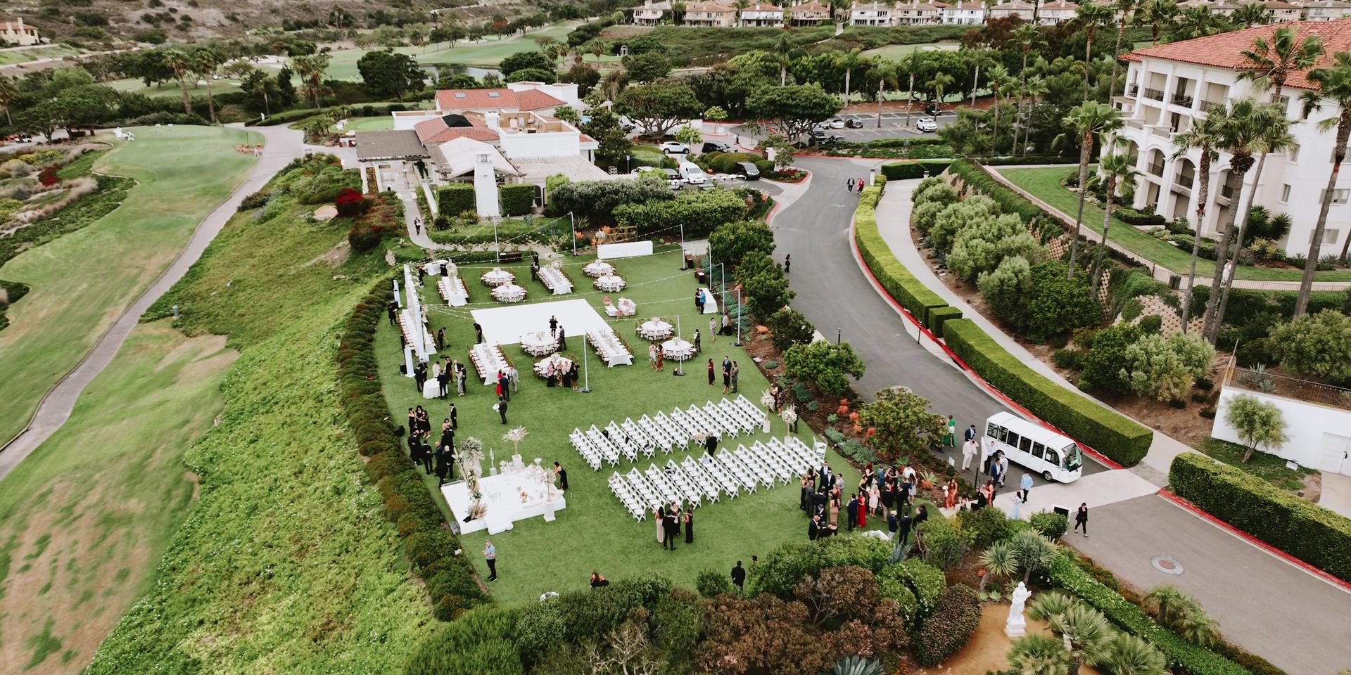 Aerial view of the ceremony lawn at Monarch Beach, white chairs in rows facing the altar with the resort and its greens spread out behind.