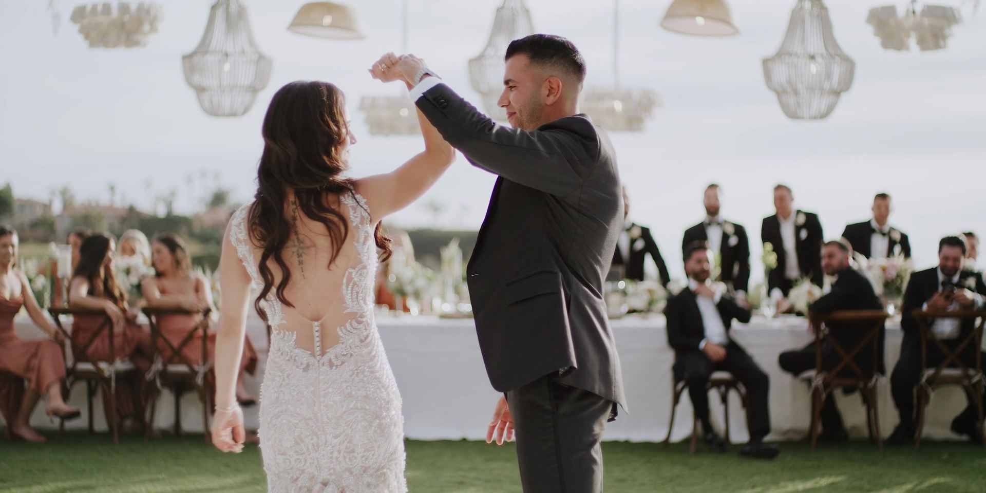 Aurash turning Madison under his arm on the dance floor, guests watching from the long table behind them.