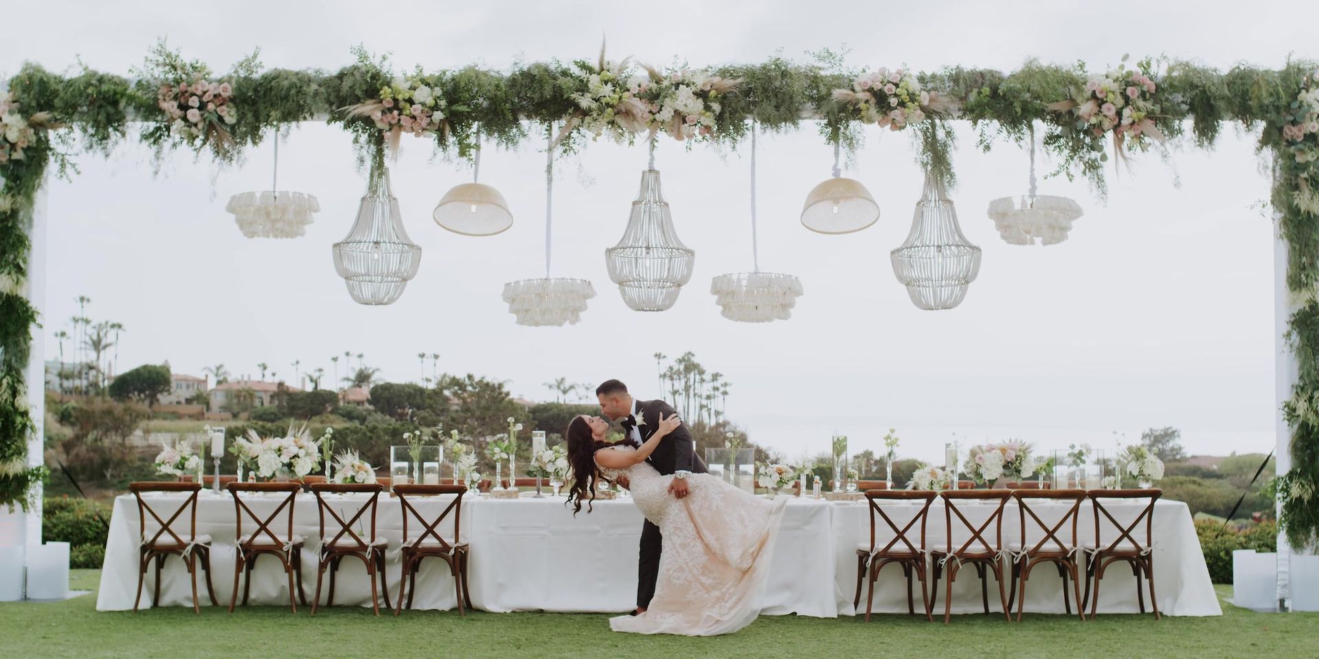 The long head table under hanging chandeliers and greenery, Aurash dipping Madison in front of it.