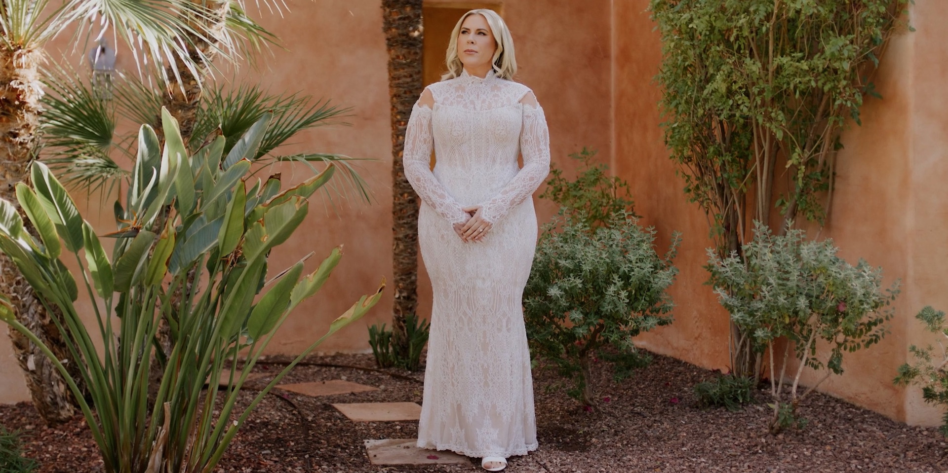 Bride at Royal Palms Resort and Spa in a lace gown, standing in a terracotta courtyard among desert palms and birds of paradise