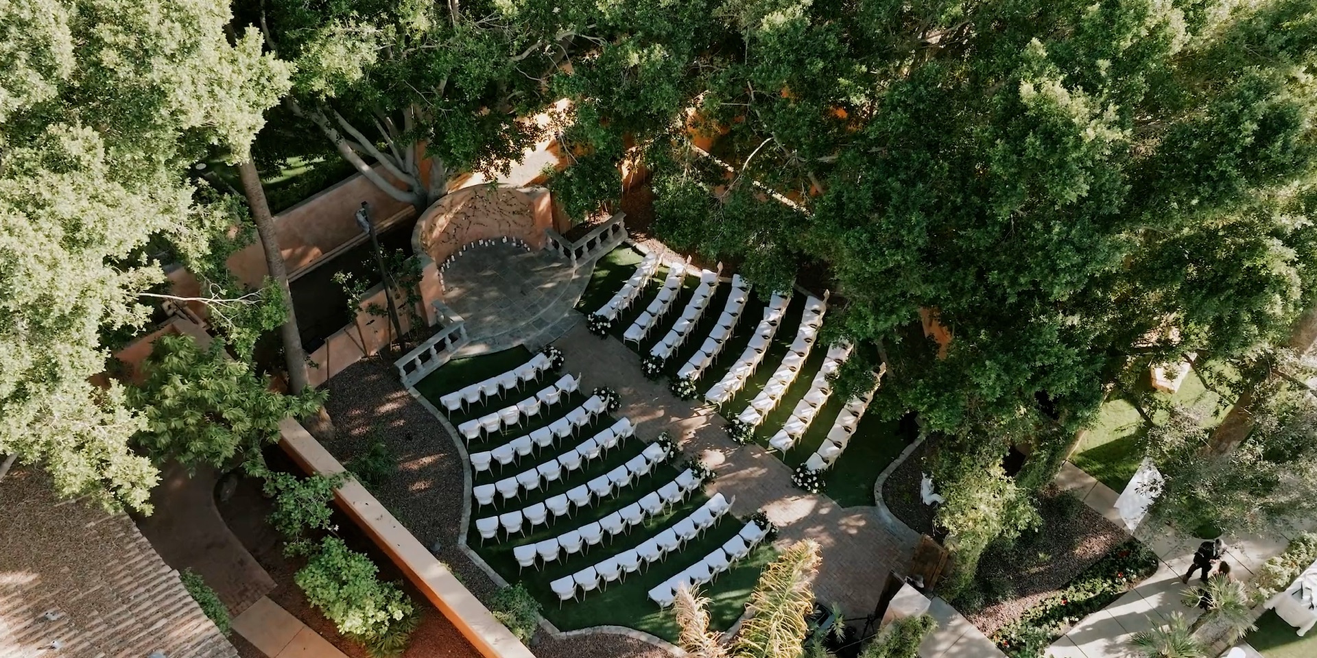 Royal Palms Resort and Spa wedding ceremony in a tree-shaded stone courtyard, white chairs arranged before the dais