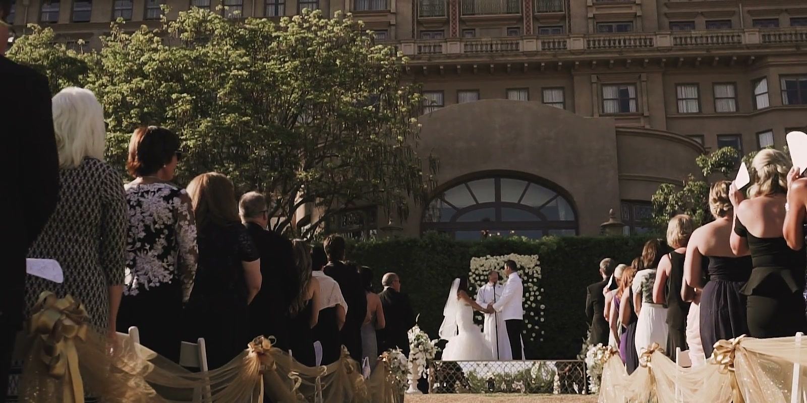 The ceremony in front of the hotel, guests standing along the aisle and an arched window behind the couple.