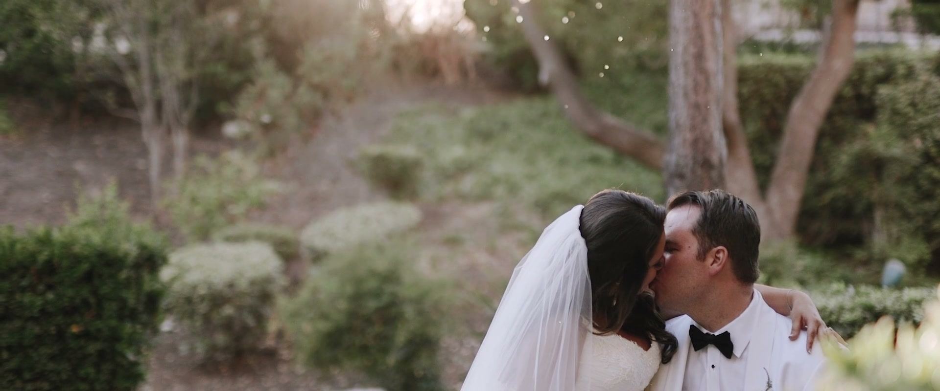 Casey and Alex kissing in a garden, her arm around his shoulders and planted slopes soft behind them.