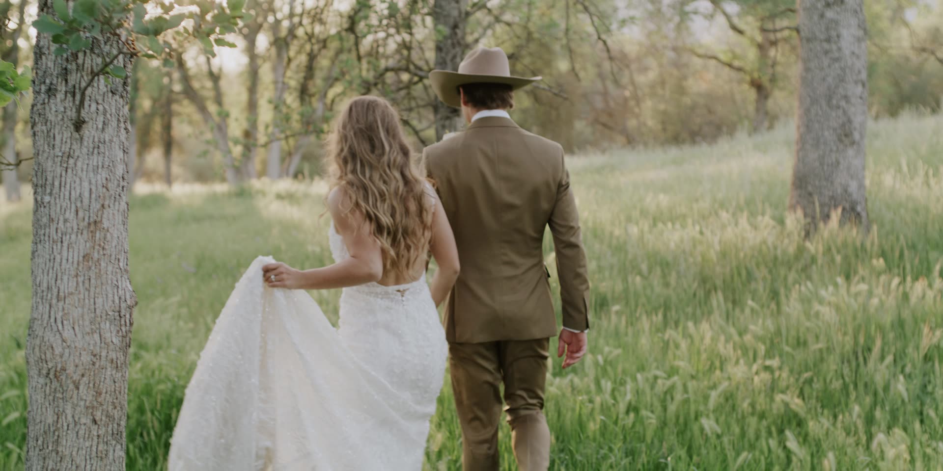 Cal and Khloe walking through the tall grass, her train trailing behind, in Kingsburg