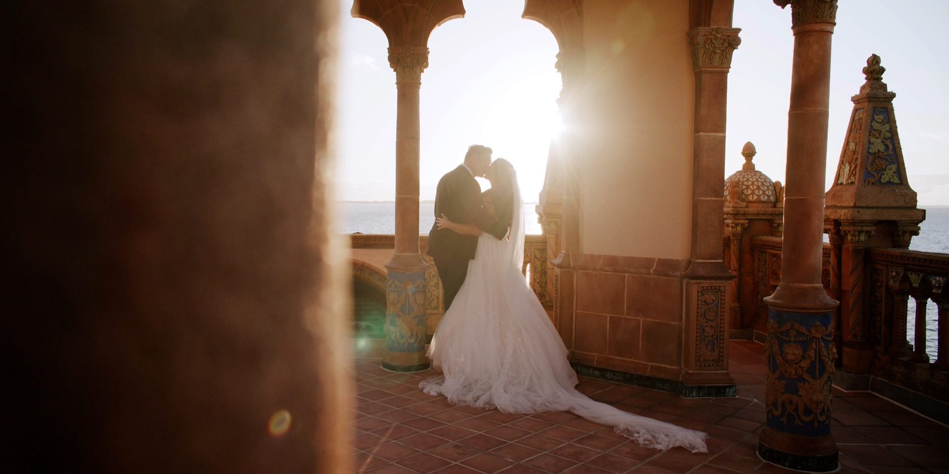 Bride and groom kissing beneath the Venetian Gothic arches of Ca d'Zan at sunset over Sarasota Bay