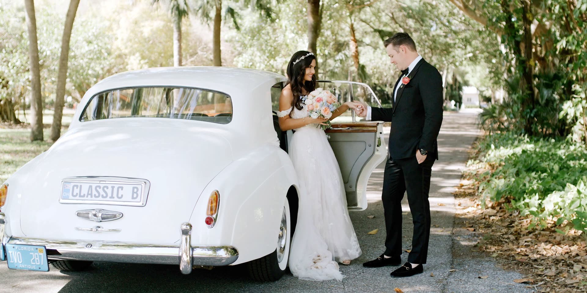 Bride and groom with a vintage white Bentley on the tree-lined drive at The Ringling in Sarasota