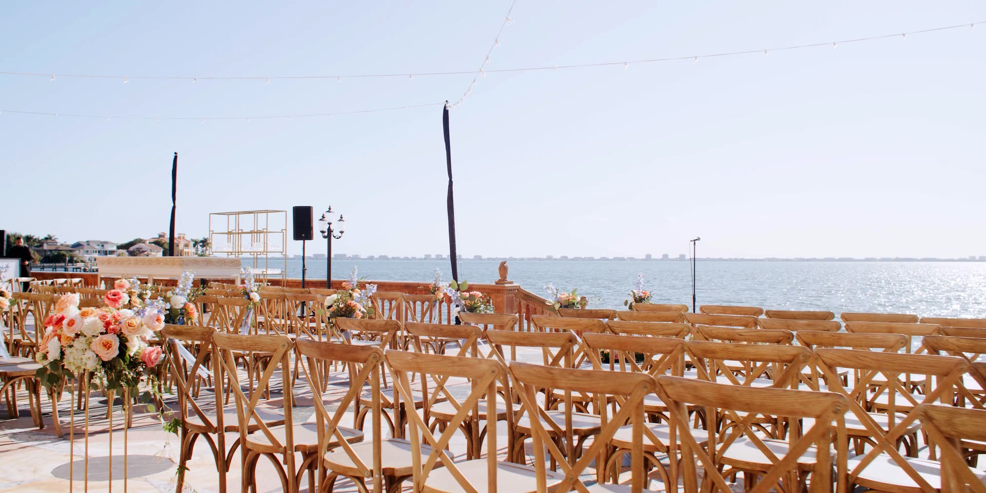 Bayfront wedding ceremony setup at Ca d'Zan in Sarasota, wooden cross-back chairs and string lights overlooking Sarasota Bay