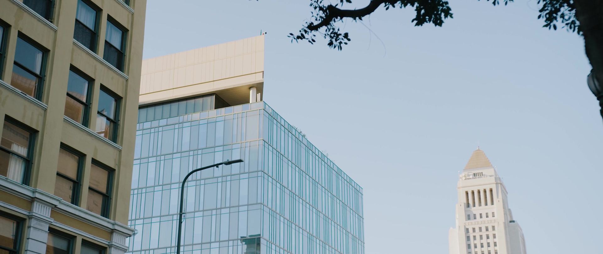 A glass office tower and an older stone building, City Hall's tower rising in the distance.
