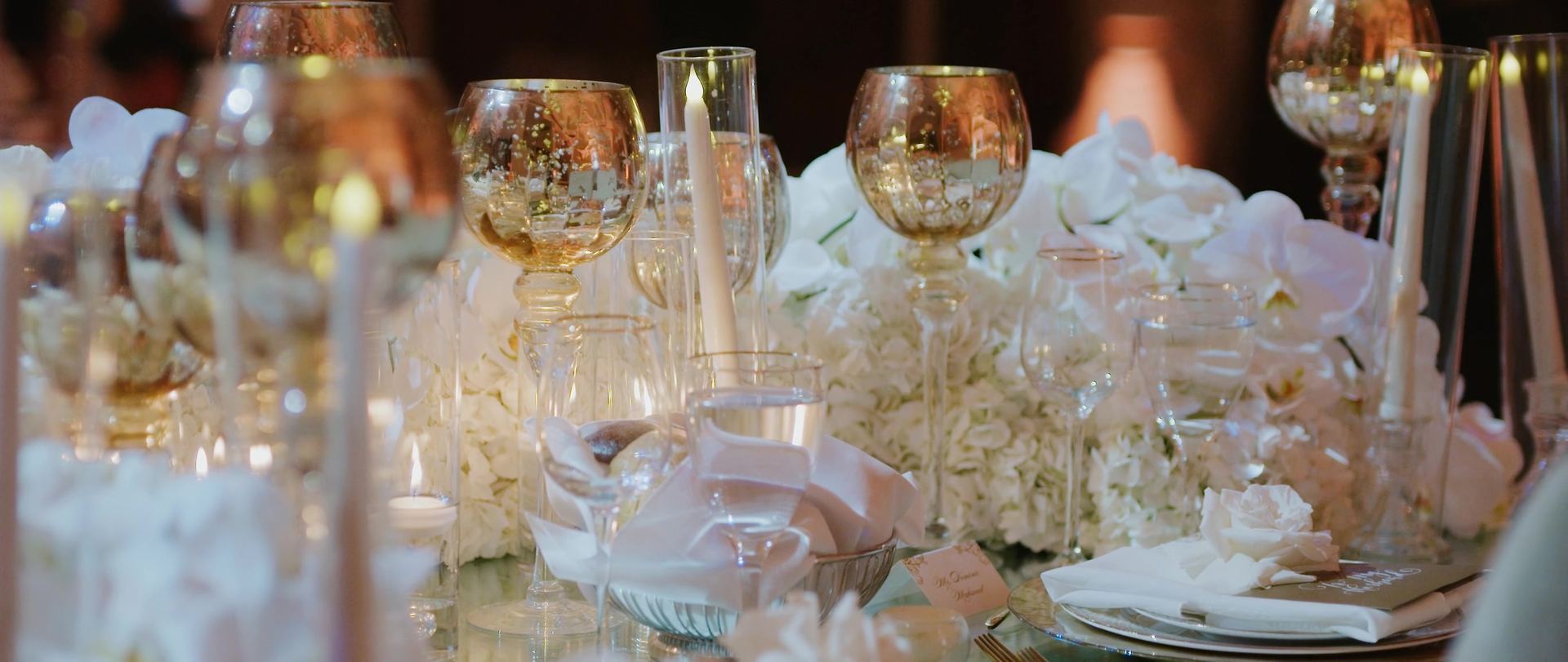 The reception tables, gold glassware and white blooms set among the candlelight.