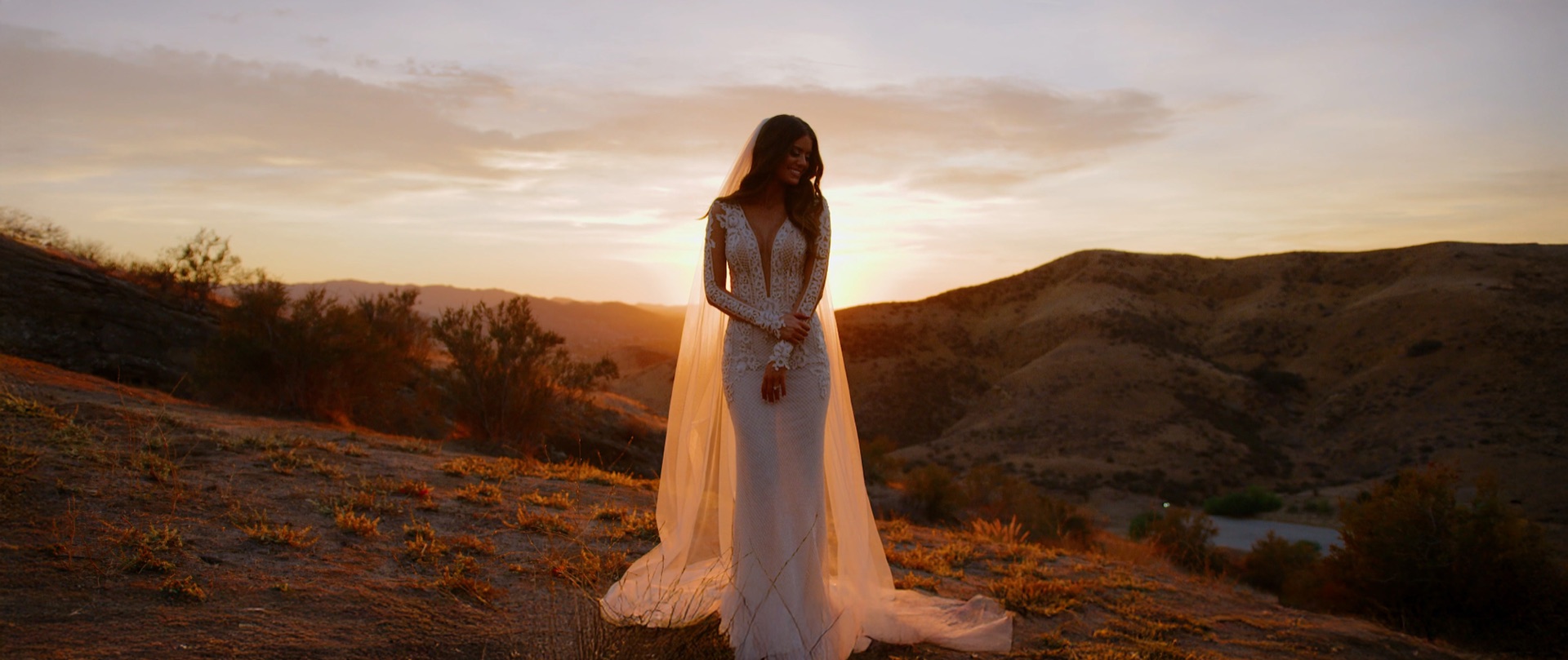 Bride Lauren alone at sunset on the Hummingbird Nest Ranch hillside, backlit in a long-sleeve lace gown and cathedral veil.