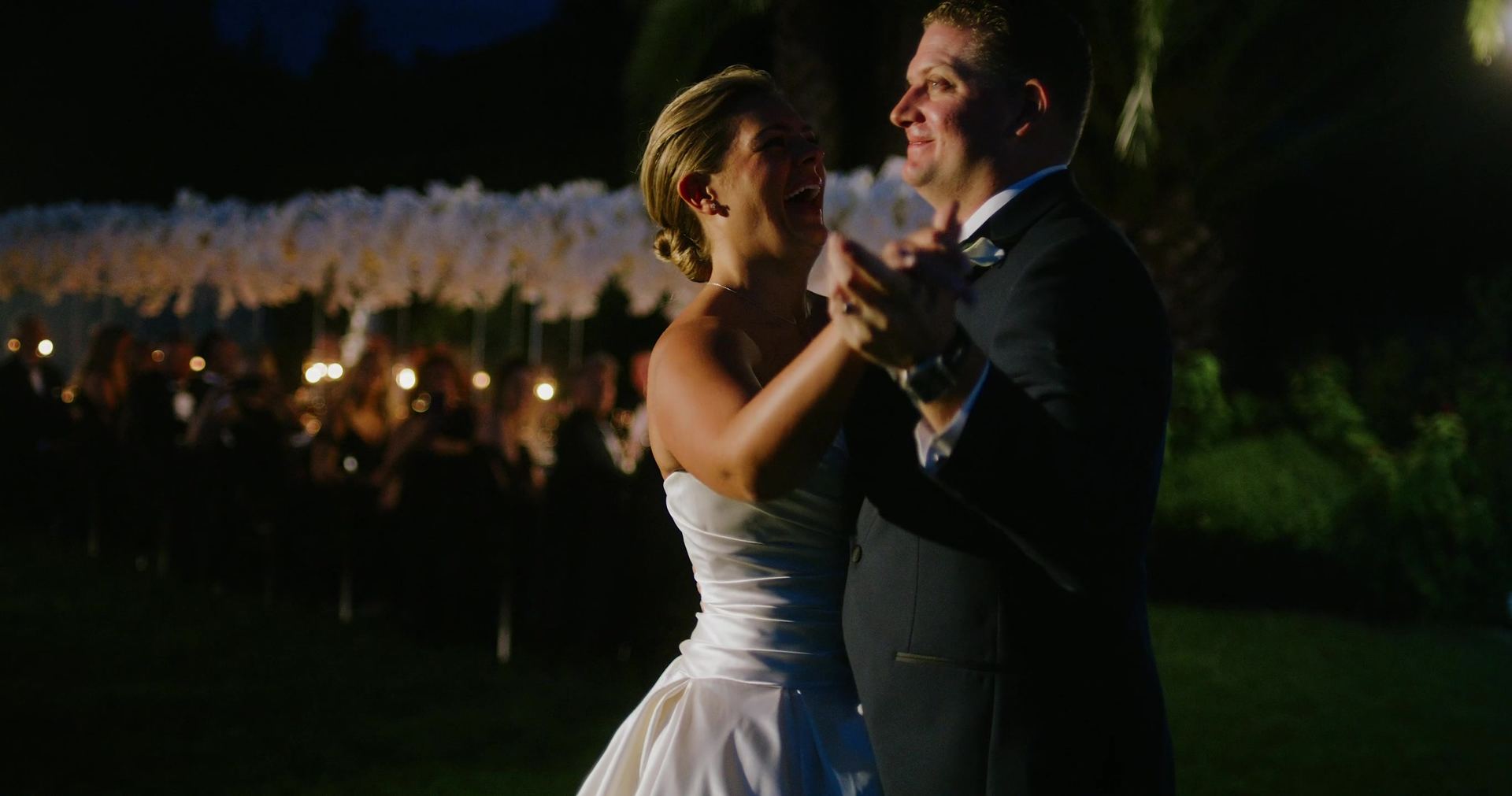 Their first dance after dark, guests and candlelit tables behind them.