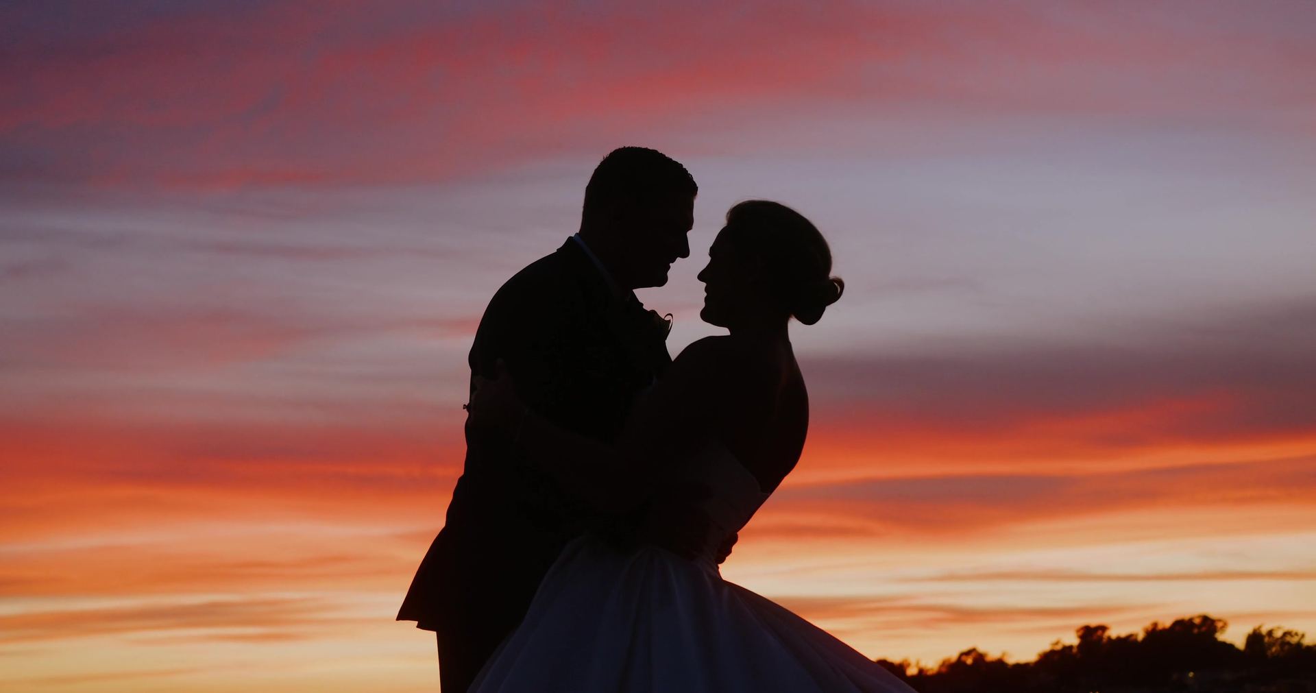 Eric and Marin in silhouette against an orange and pink sky.