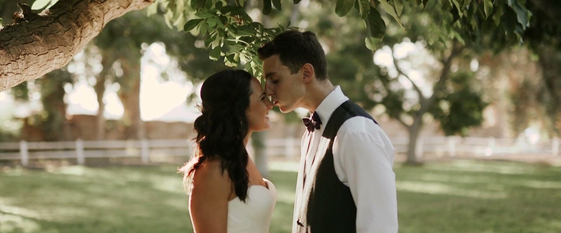 Alex and Lindsay close together under the branches of a walnut tree, a white fence and lawn behind them
