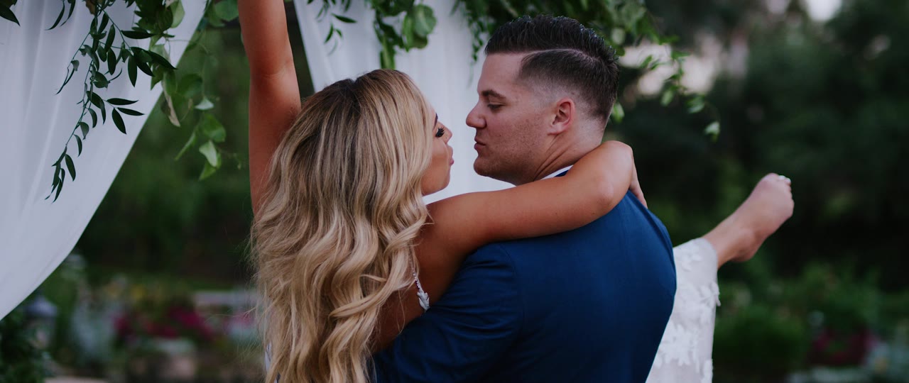 Brandon and Erin embracing under the greenery of their ceremony arch at Lake Oak Meadows in Temecula