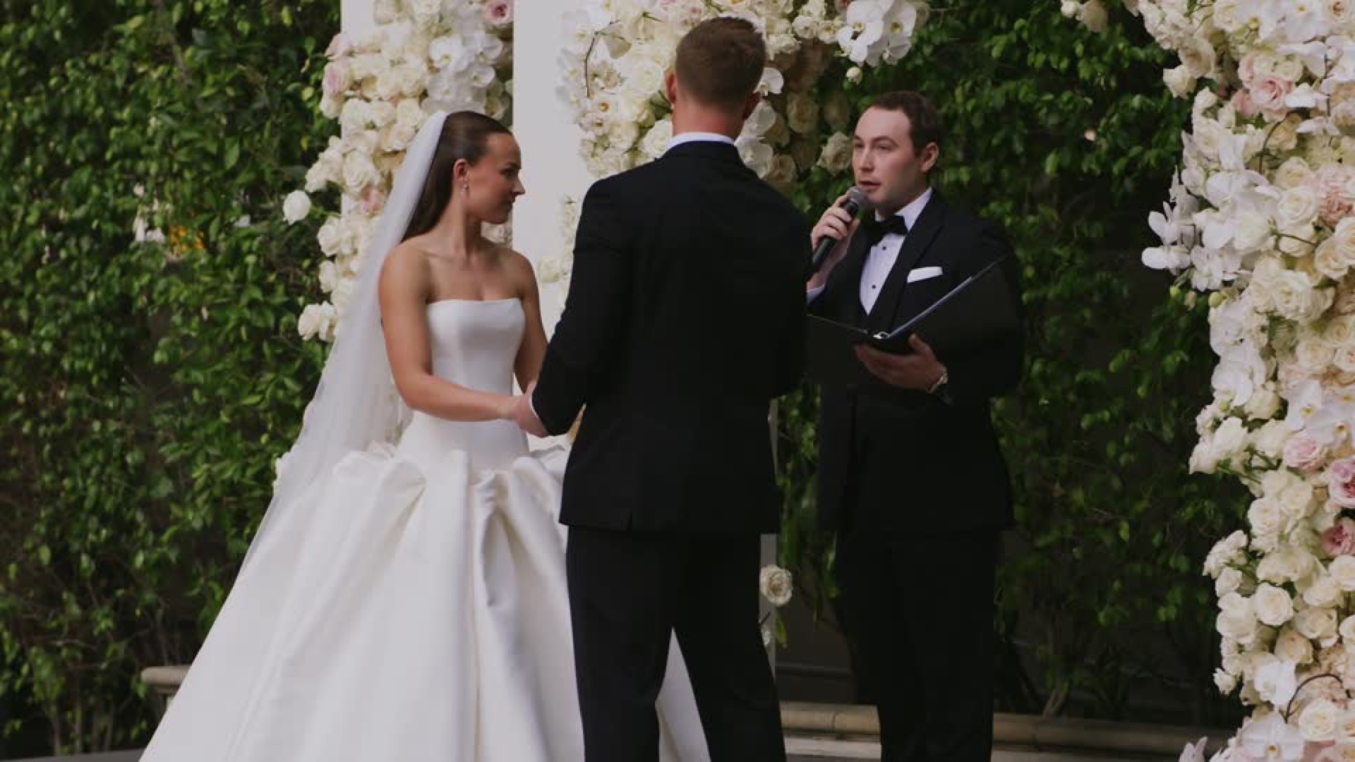 Brian and Ryan being walked down the rose-lined aisle at their wedding ceremony