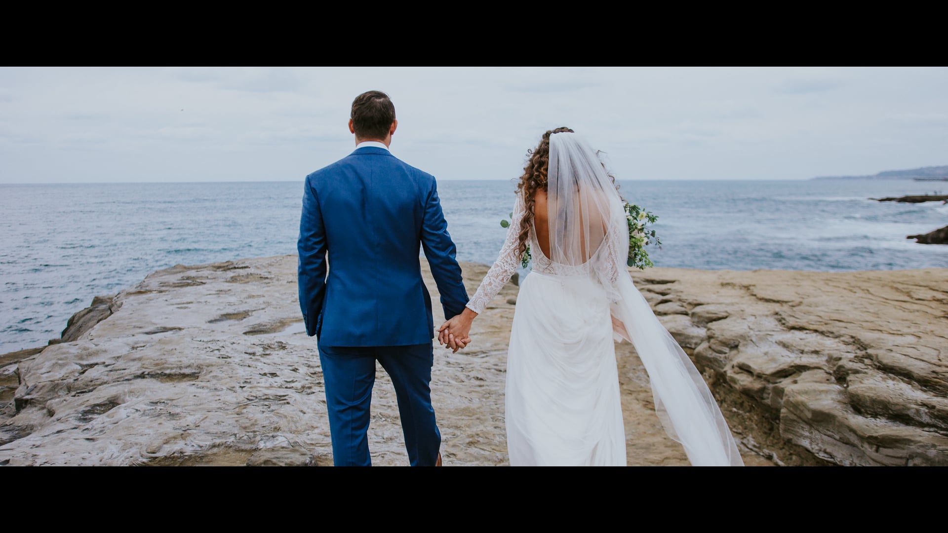 Dani and Shane walking hand in hand across the tide rocks on the San Diego coast