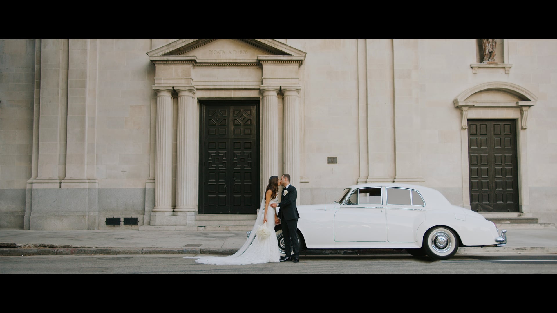 Desiree and Dominic beside a white vintage car outside the church in Los Angeles