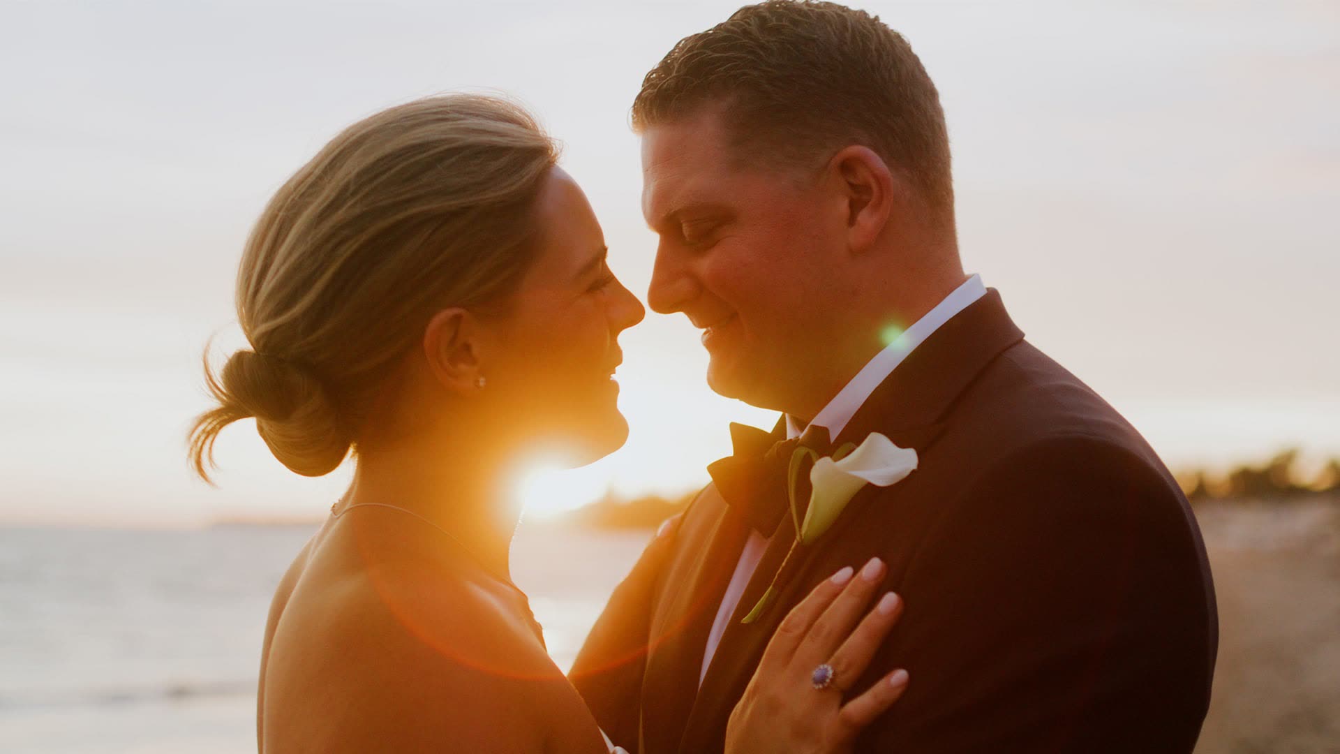 Eric and Marin nose to nose in Montecito, California, the setting sun flaring directly between them, Eric in a rust brown suit.