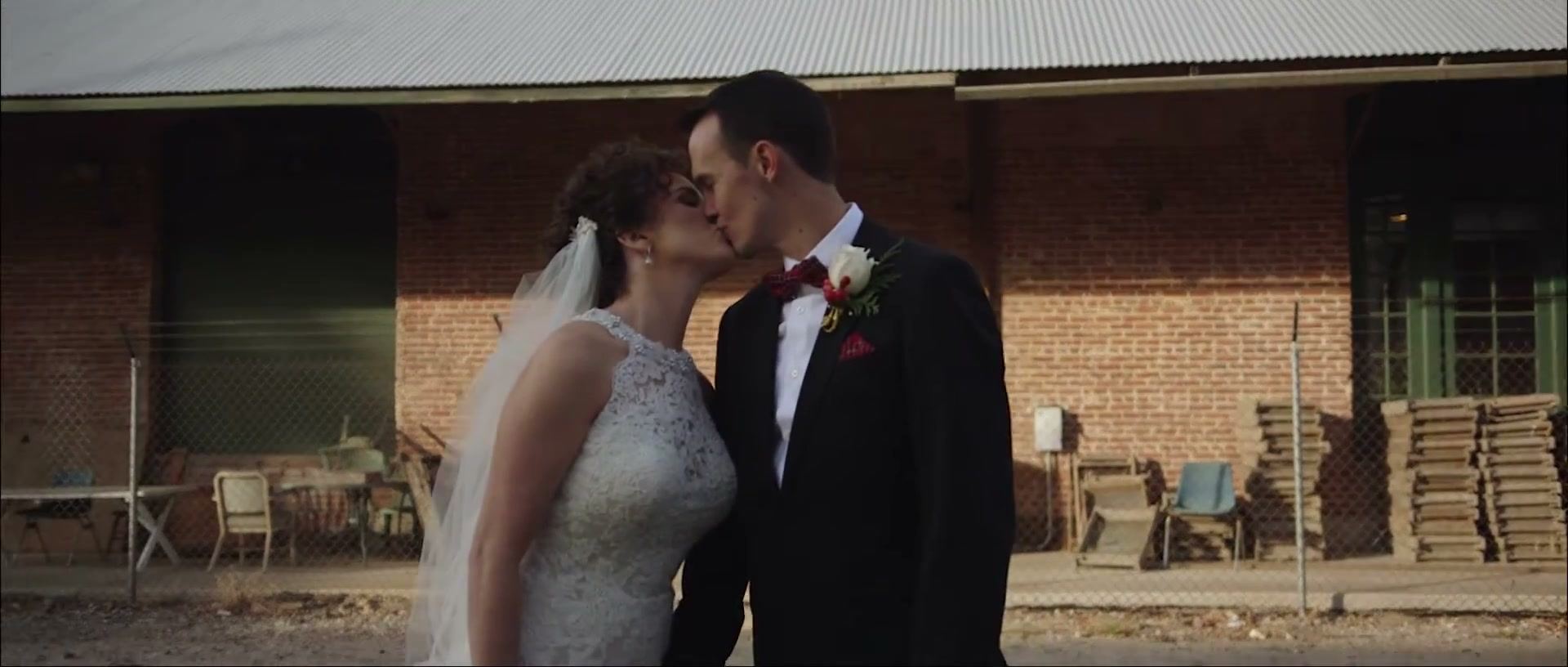Hayley and Brandon kissing in front of an old brick building with green-framed doors