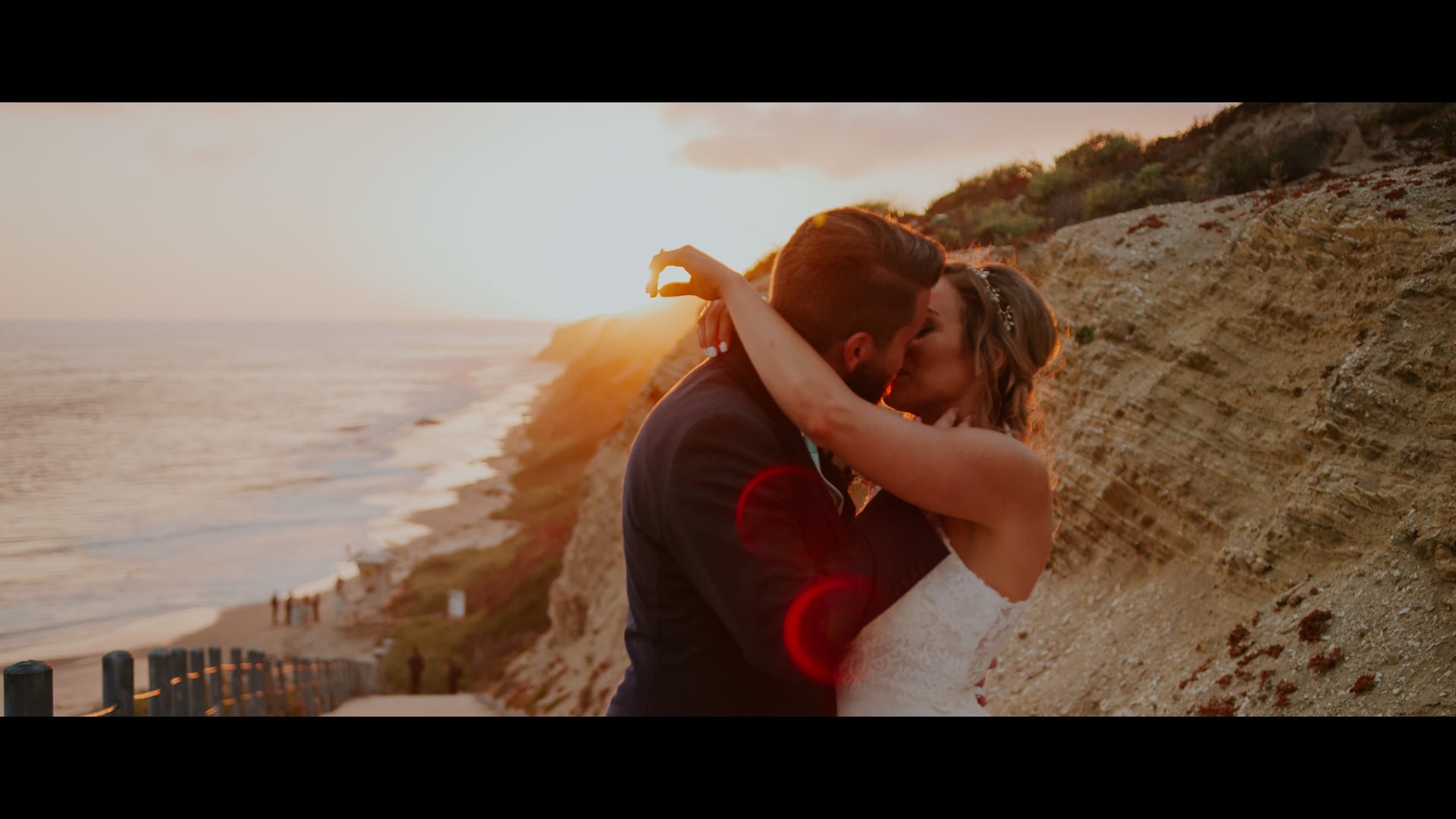 Josh and Shayna kissing on the bluffs at Newport Beach with the sun going down behind them