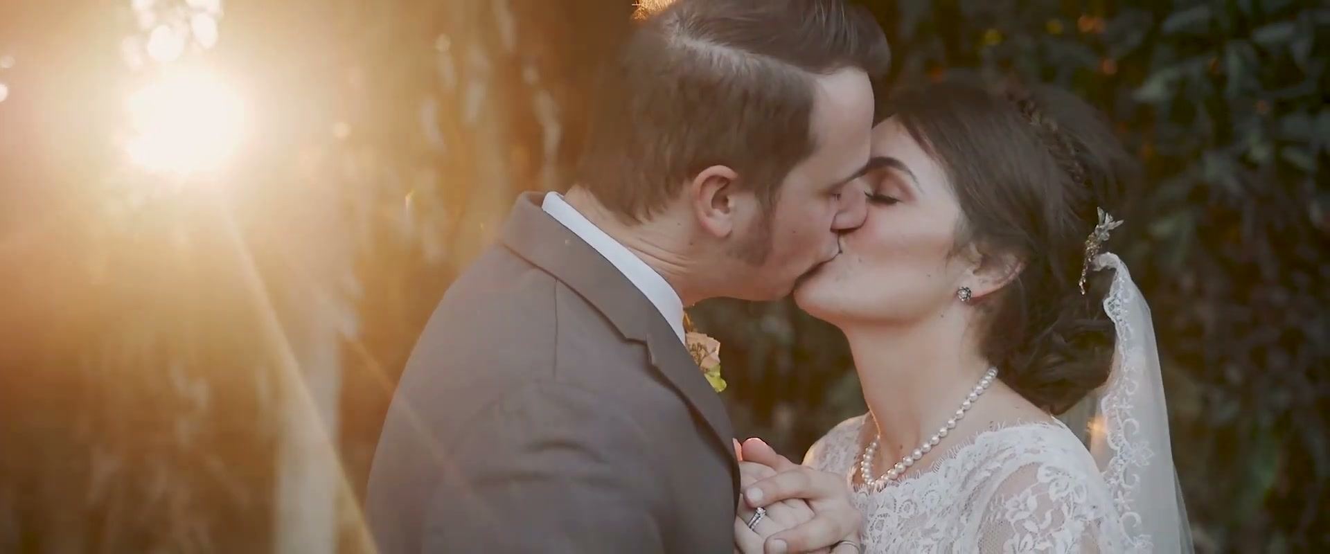 Nick and Danielle kissing in warm low sun, light flaring through the leaves behind them
