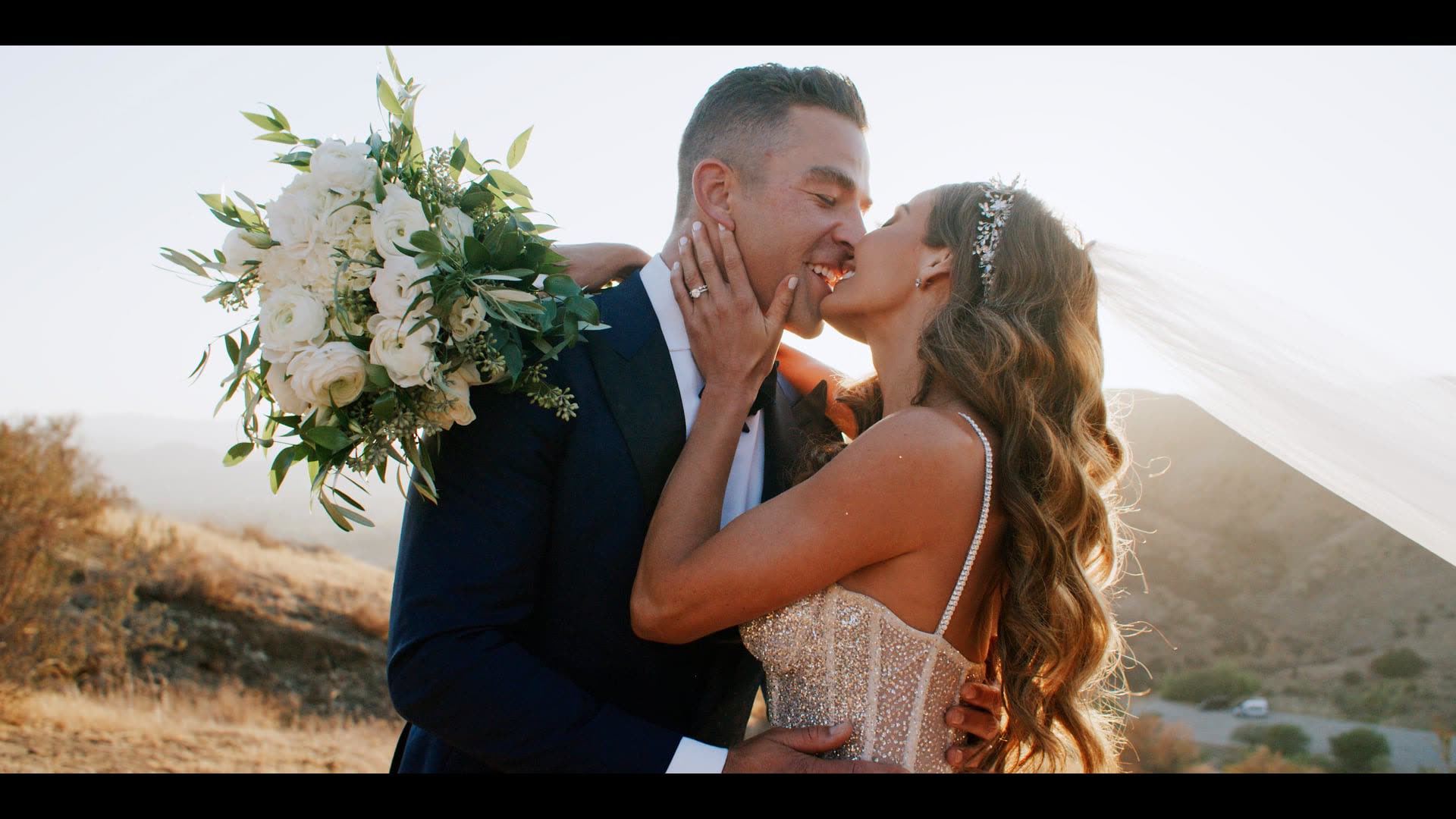 Sean and Lindsey kissing on the hillside at Hummingbird Nest Ranch, her bouquet held between them