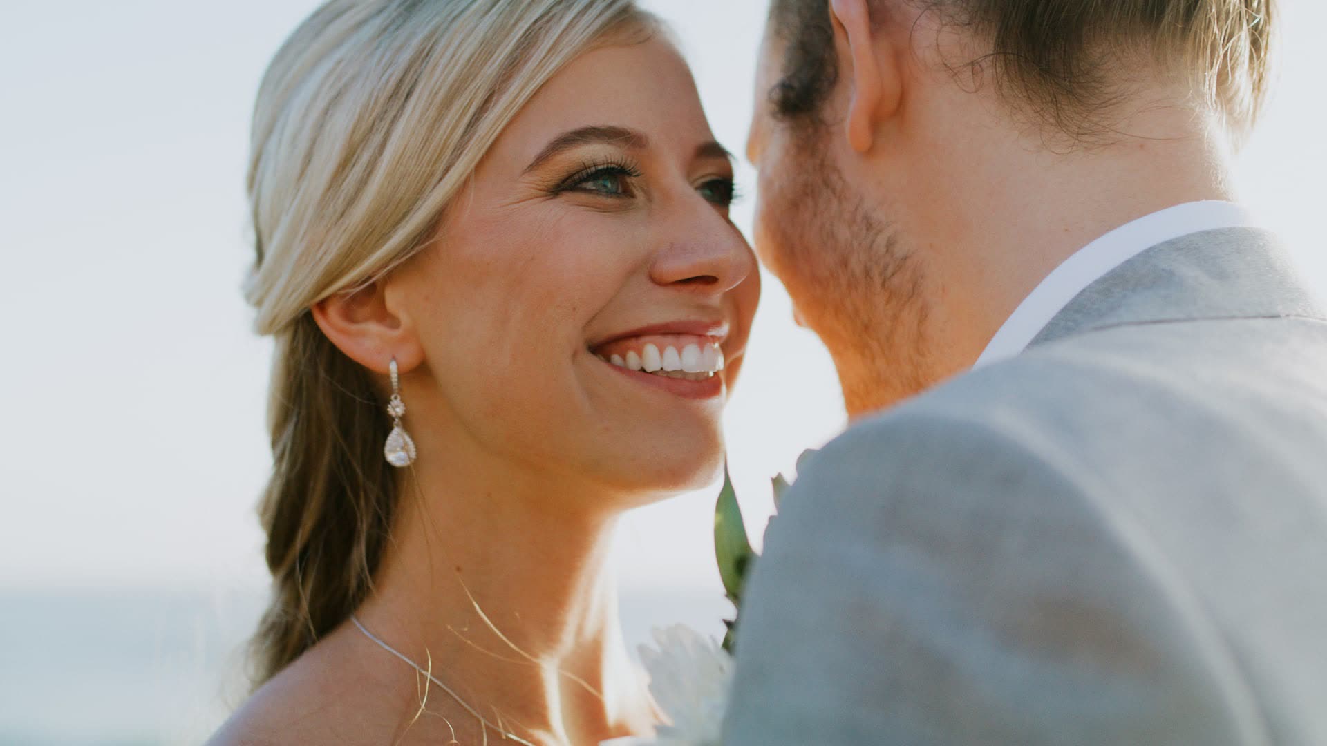 Zoe and Mitch close together on the La Jolla coast, she is laughing, he is in a light suit, shallow focus