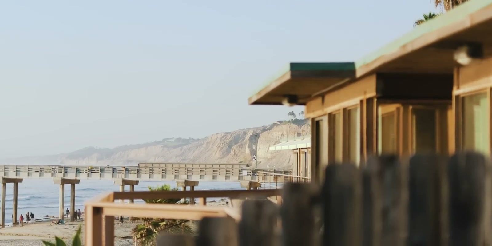Scripps Pier and the bluffs beyond it, seen past a wooden roofline.