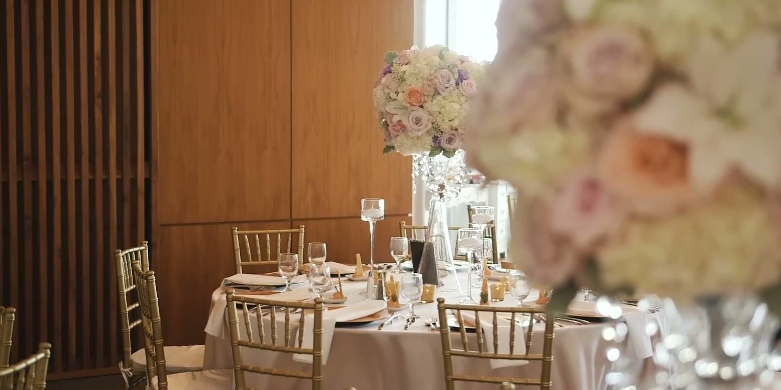 Reception tables set inside the Forum against its slatted wood wall, with a tall arrangement of pale roses.