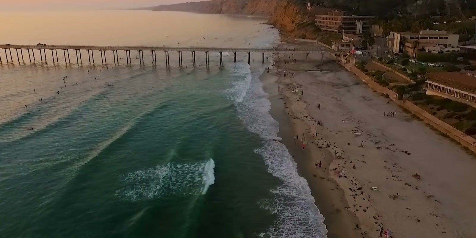 Scripps Pier and the beach from above in low evening light, surfers in the water beside the pier.