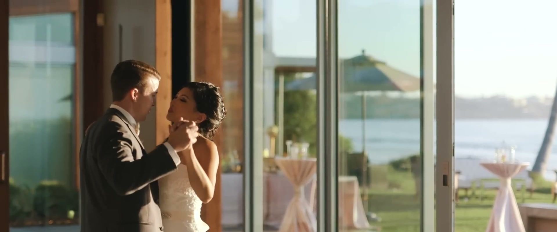 Gina and Jeff dancing inside the Forum beside its glass wall, the lawn, cocktail tables and the ocean soft beyond the glass.