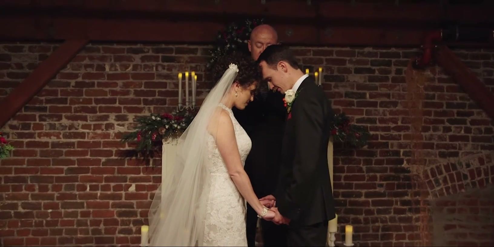 Hayley and Brandon holding hands before the officiant against the brick wall, candles on either side.