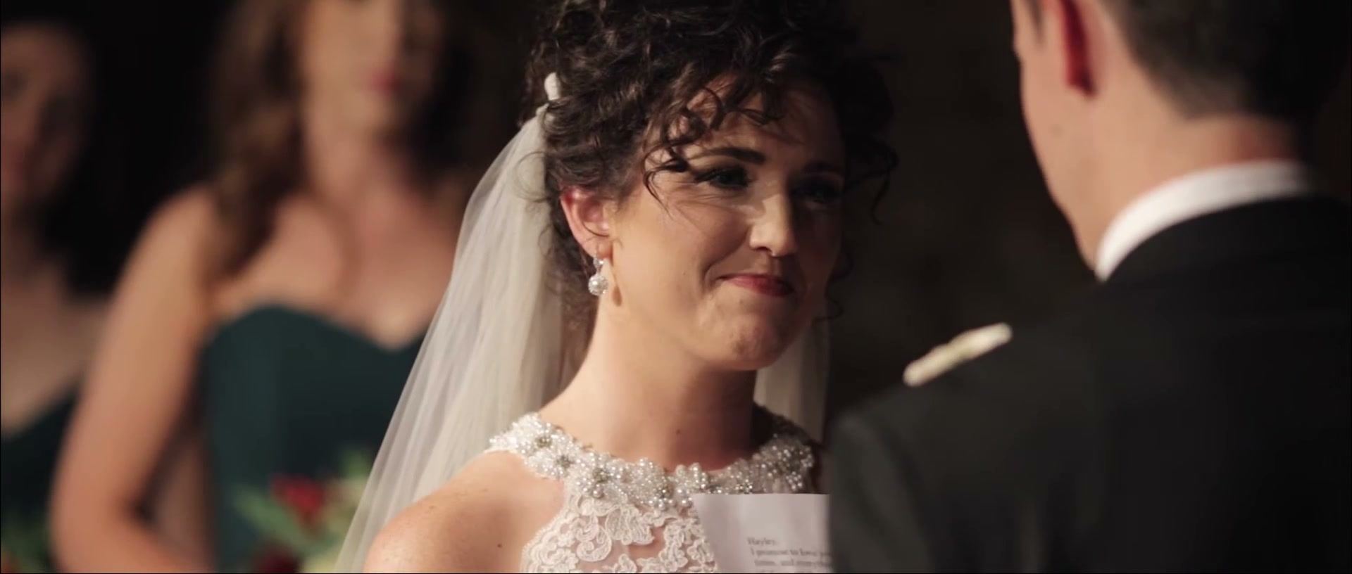 Hayley smiling through tears as she faces Brandon, a bridesmaid in green soft behind her.