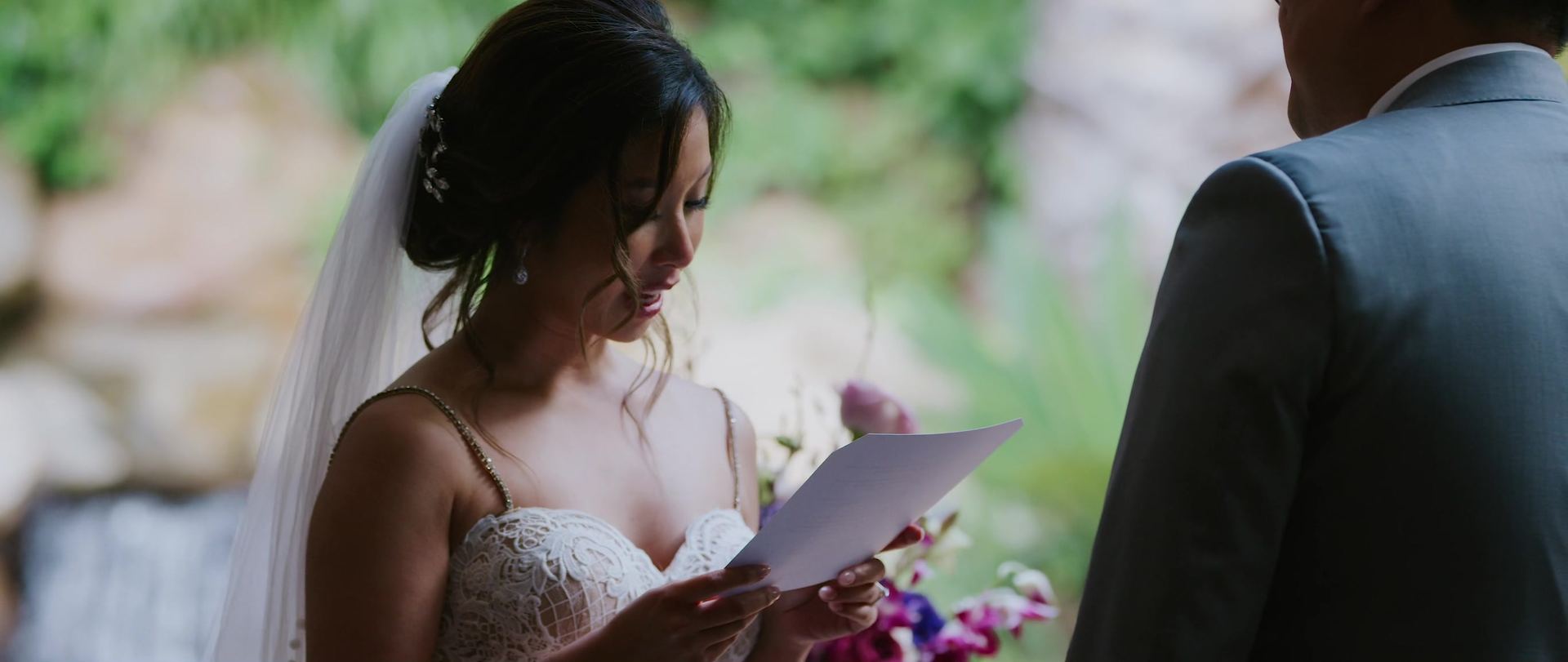 Helen reading her vows aloud from a card, her veil pinned back.