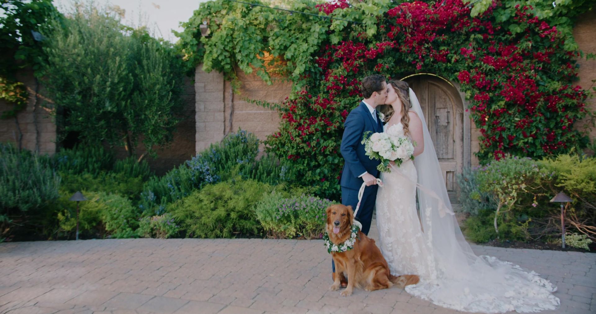 Hudson and Tiffany with their dog at the arched door, bougainvillea spilling over the wall behind them.