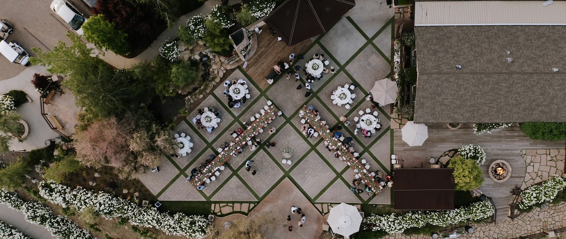 The reception from directly overhead, two long tables and round tables set on a grid-patterned patio with umbrellas around the edge.