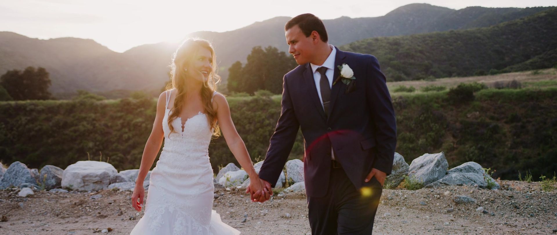 Jonathan and Breanna walking hand in hand along a rocky path, the sun low behind the hills.