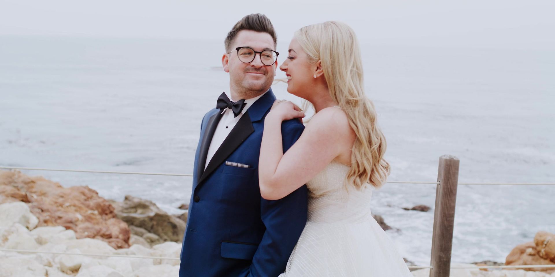 Gina with her hands on Josh's shoulder at a cable fence above the rocks and ocean at Terranea Resort