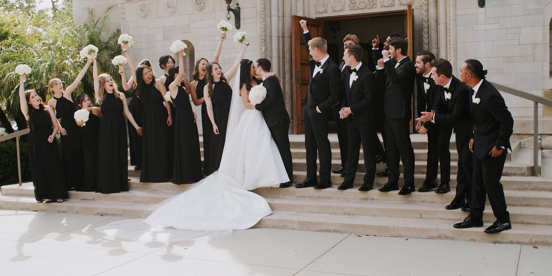 The wedding party on the church steps, bouquets lifted overhead.