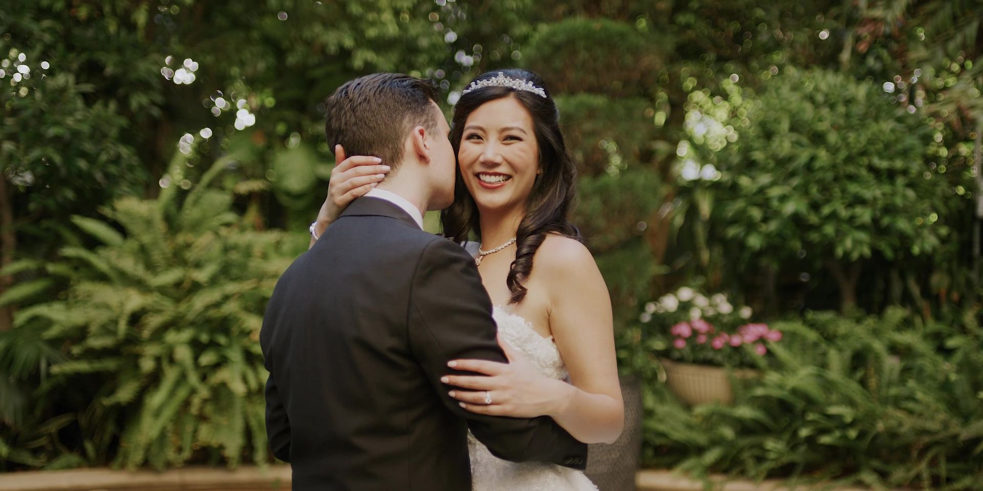 Joe kissing Jessica's cheek in the garden, ferns behind them.