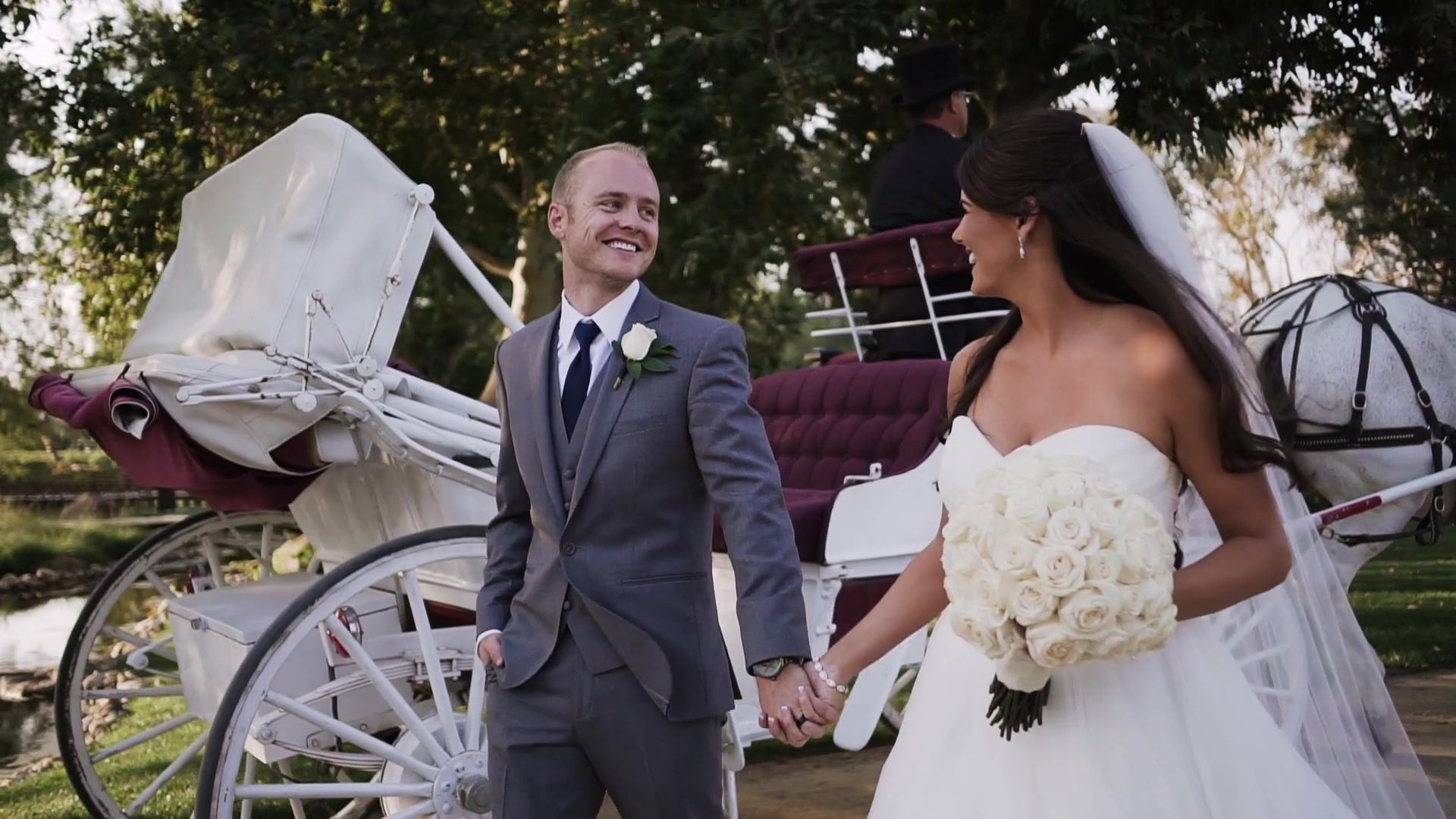 Josh laughing with Jade beside the white carriage, her bouquet of white roses in hand and a coachman at the carriage behind.